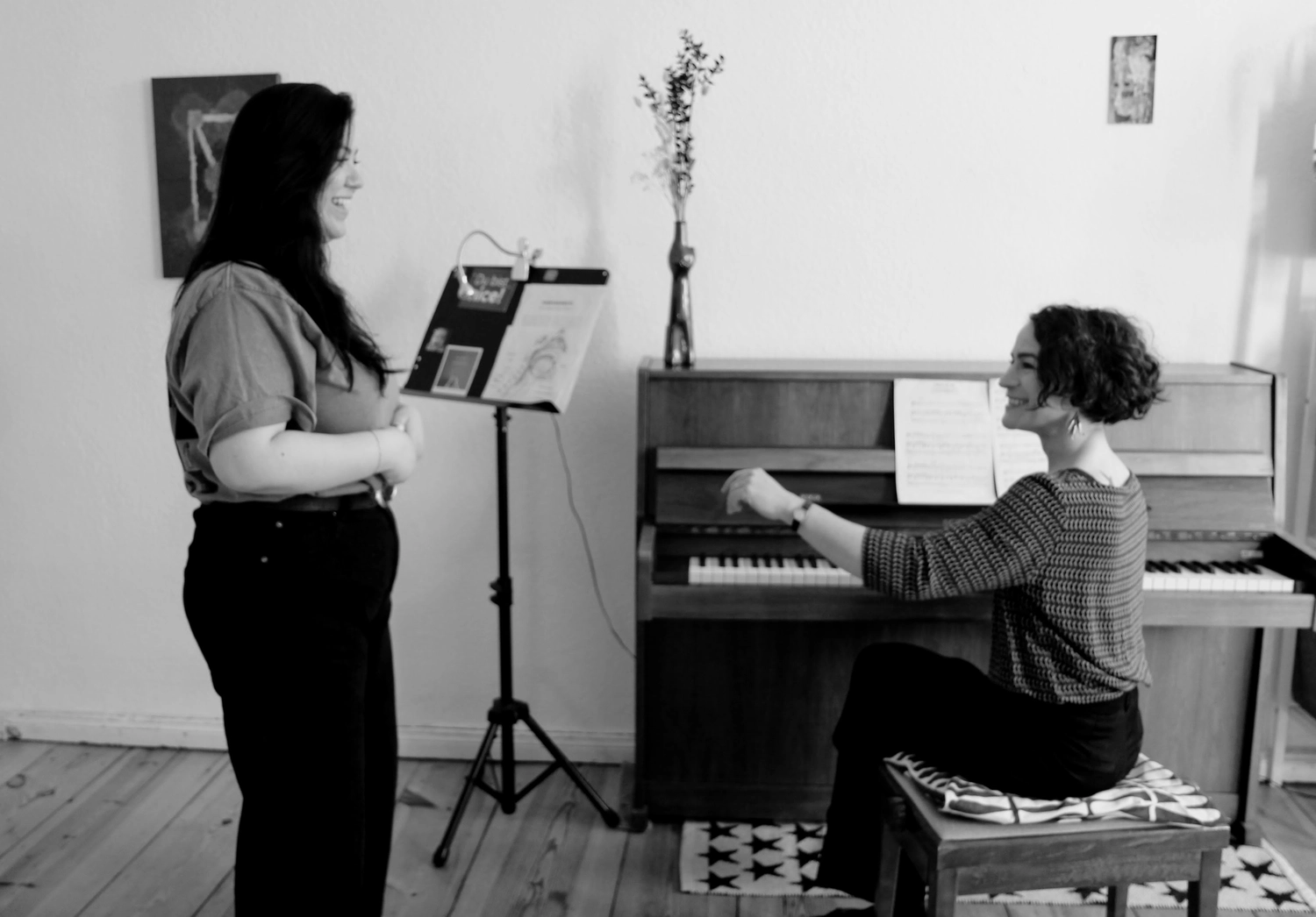 Aliénor Bordes - Stimme & Entfaltung - Ein Schwarzweißfoto, das eine stehende und eine sitzende Frau an einem Klavier in einem Zimmer zeigt.
